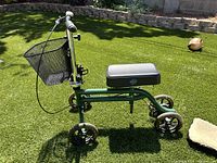 Side view showing green metal frame knee scooter with black padded seat and front wire mesh basket.