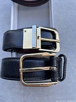 Top view of two black leather men's belts with gold-tone buckles showing wear.