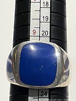 Front view of men's ring showing square lapis lazuli stone with a small ding on surface, band size visible on ring sizer, polished sterling silver band.