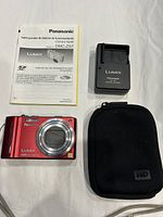 Panasonic Lumix DMC-ZS7 camera, user manual in Spanish, battery charger, and black WD carry case shown on flat surface.