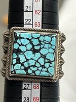 Close-up photo showing the square turquoise stone with black matrix and twisted rope bezel setting on the sterling silver ring.