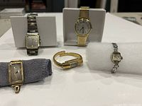 Overview of five vintage watches on display showing worn condition, including two men's watches and three ladies' watches with various face shapes, bands, and colors