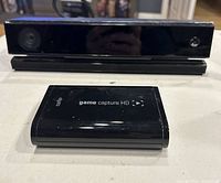 Front view of Microsoft Xbox Kinect sensor and Elgato Game Capture HD device together on table.