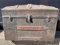 Front view of the 1800s steamer trunk showing leather texture, metal locks, and wooden slat on the front.