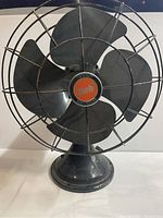 Front view of antique Diehl Manufacturing Co. electric fan showing four large black metal blades and protective wire cage. Base and central hub with logo visible.