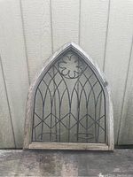 Full view of gray weathered wooden arch window frame with black metal gothic design and two circular metal rings for plants.