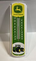 Front view of John Deere metal thermometer with temperature scale, logo, and tractor image.