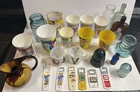 Photo showing assortment of vintage glass jars, ceramic pitcher, collectible cups, and small glass insulators and bottles