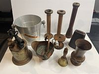 Photo showing a variety of small vintage metal items arranged on a white background including a small branded metal bucket, wooden candle holders, a wooden grinder, bell, and copper bucket with ceramic handle.