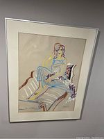 Framed oil pastel drawing showing a seated woman on a chaise lounge with signature in bottom corners.