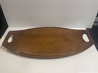 Top view of the wooden surfboard-shaped serving tray showing the smooth medium brown polished surface and two rectangular cut-out handles.