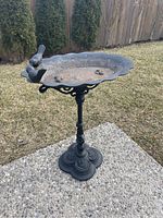 Full view of vintage cast metal bird bath standing on outdoor ground surface. Ornate design with birds on the rim visible.