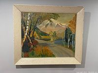 Front view of vintage oil on board landscape painting in cream frame showing autumnal trees, road, mountains, and lake.