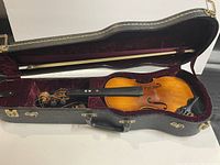 Open black violin case showing violin and bow inside with red velvet interior lining