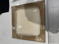 Close-up photo showing the ceramic plate with a square shape, concentric ridges and a gradient brown to cream finish.