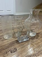 Four clear glass vases arranged on wooden floor showing different shapes and sizes.