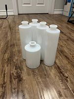 Five white porcelain vases of varying heights grouped together on wooden floor.