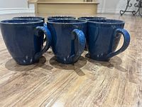 Six blue ceramic coffee mugs arranged in two rows, showing exterior sides and handles. The mugs are around 4 inches tall with a glossy blue finish.