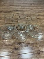 Seven clear glass vases displayed on wooden floor: three tall with wide flared openings and four round globular ones.