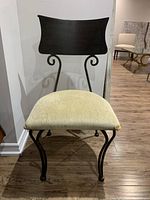 Front view of one iron frame dining chair showing cream upholstered seat and curved dark wood backrest with scroll iron detailing on legs.