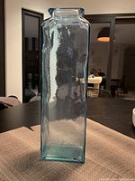 Tall rectangular blue glass vase placed on a table with textured surface visible.