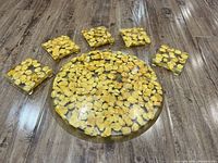 Round clear cake serving plate centered surrounded by six square clear coffee coasters, all with yellow leaves embedded.