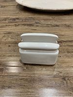 White ceramic napkin holder with square base and curved napkin slot on wood surface.