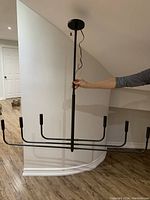 Front view, chandelier extended configuration, held by hand under ceiling canopy