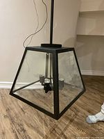 Full view of the trapezoidal iron and glass chandelier showing clear glass sides and four candle-style light sockets inside.