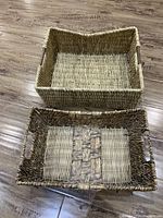 Two natural fiber woven rectangular baskets displayed on wood flooring. Larger basket has a consistent light tan weave; smaller basket has patterned center and darker woven edges.