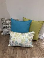 Photo showing four decorative pillows including typography print, two solid color, and one floral pattern pillow.