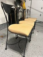 Four IronAge dining chairs with black iron frames and beige cushions showing side perspective of chairs.