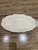 Top view of a large white oval serving plate with scalloped edges on a wooden floor.