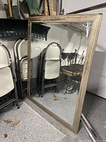 Full view of the rectangular mirror leaning against the wall showing the wood frame and clean reflective glass surface.