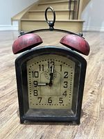 Front view of Pottery Barn antique style alarm clock with visible clock face and red alarm bells on top.