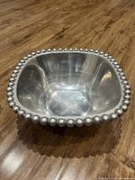 Silver serving bowl placed on wooden floor, showing side view and beaded edge detail.