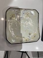 Top view of single square ceramic sushi plate showing floral design and dark brown edge.