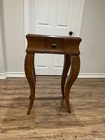 Front and angled view of wooden side table showing ornate curved legs and drawer, highlighting scratches and wear on legs and wood surface.