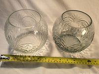 Two clear glass bowls or vases placed side by side with a measuring tape showing approximately 6 inches diameter.