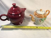 Two teapots side by side with measuring tape showing size