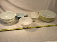 Collection of four Pyrex mixing bowls and one white glass mixing bowl with a measuring tape in front showing sizes.