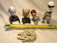 Group photo of five Star Wars themed figures with tape measure for scale; includes characters and vehicle model.