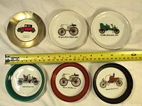 Front view of 6 small round car-themed coasters/dishes with a measuring tape showing 3 3/4 inch diameter