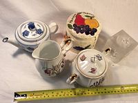 Group photo showing all four ceramic items and the glass candle holder with a measuring tape for scale
