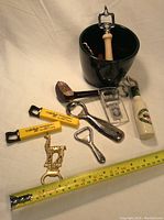 Eleven bar and bottle opener items arranged including black ice bucket and various bottle openers of metal and plastic.