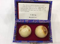 Two ivory-colored spherical balls with natural brown spots inside a blue decorative box with red interior, under the lid an instruction card describing usage of Healthy Balls.