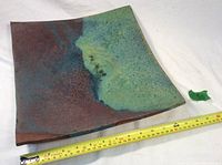 Square ceramic plate with blended green, blue, and brown glaze on flat white surface with measuring tape showing approx 12.5 inch width.