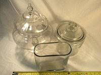 Three clear glass candy dishes of varying shapes and lids photographed together on a white background with a measuring tape.