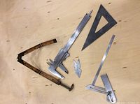 Five machinist tools displayed on wood surface: vintage folding wooden ruler, metal vernier caliper, metal triangular square, adjustable square, and pocket ruler.