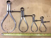 Four outside calipers laid side by side with a measuring tape below showing their lengths from about 4.5 to 9 inches.
